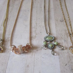 May include: A selection of necklaces and earrings. The jewellery includes gold earrings with purple teardrop stones, a gold necklace with interlocking rings, and a silver necklace with a green pendant.