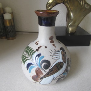 May include: A white ceramic vase with a round body and a narrow neck. The vase is decorated with hand-painted blue, green, brown, and white floral and bird designs.