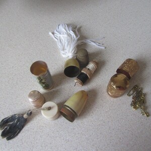 May include: A collection of vintage thimbles, spools of thread, and a small sewing kit. The thimbles are made of metal and have a gold finish. The spools of thread are made of wood and have a white finish. The sewing kit is made of metal and has a white and blue finish.