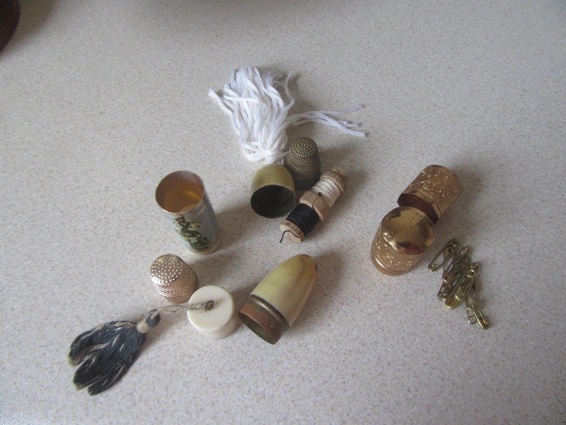 May include: A collection of vintage thimbles, spools of thread, and a small sewing kit. The thimbles are made of metal and have a gold finish. The spools of thread are made of wood and have a white finish. The sewing kit is made of metal and has a white and blue finish.
