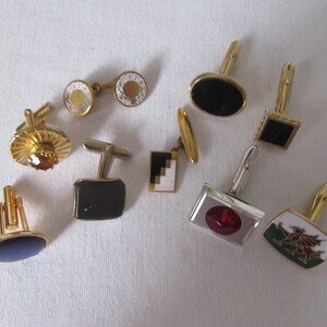 May include: A collection of various cufflinks with gold and silver tones. Designs include black, red, and white stones, geometric patterns, and a Welsh dragon emblem. The cufflinks are displayed on a white surface.