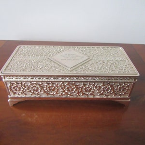 May include: Silver keepsake box with an ornate floral design. The lid has a diamond-shaped plaque with the inscription "In honour of your happy 50th birthday Lots of love from John, Anne".