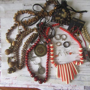 May include: A selection of necklaces, earrings, and rings in various styles. The necklaces feature beads in red, brown, and gold tones. Earrings and rings are silver and black. A small black bag with the text "Victoria's Secret" is also present.