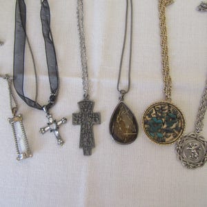 May include: Seven silver and gold necklaces with various pendants, including a cross, a teardrop, a round pendant with a floral design, and a pendant with a small figure.