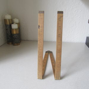 May include: A wooden folding ruler with brass accents. The ruler is closed and standing upright on a white surface. The ruler has markings in inches.