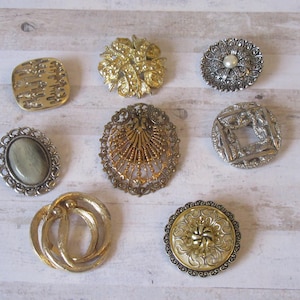 K&ouml;nnte beinhalten: Sortiment von acht Vintage-Broschen in Silber- und Goldt&ouml;nen. Die Broschen zeigen eine Vielzahl von Designs, darunter florale, geometrische und abstrakte Muster. Einige Broschen haben einen Perlen- oder Steinakzent.