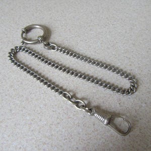 May include: A silver pocket watch chain with a round clasp and a hook at the end.