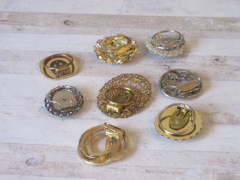 K&ouml;nnte beinhalten: Acht Ohrringverschl&uuml;sse im Vintage-Stil in Gold- und Silbert&ouml;nen. Die Verschl&uuml;sse sind alle in verschiedenen Stilen gehalten und weisen komplizierte Designs auf.