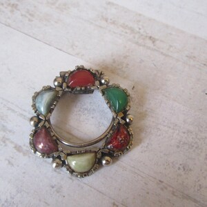 May include: A silver ring with six different colored stones set in the metal. The stones are green, red, and white.