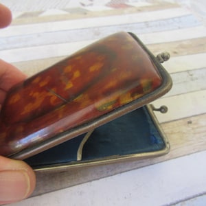 May include: A vintage rectangular coin purse with a tortoiseshell pattern on the lid. The purse has a metal frame and opens to reveal a blue interior. The purse is held open, showing the inside.
