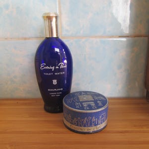 May include: A blue glass bottle of Evening in Paris toilet water by Bourjois. The bottle has a silver cap and white lettering.  A blue and silver round tin of Evening in Paris is also pictured.
