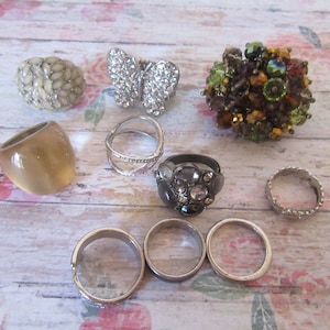 Op de afbeelding: Assortiment van ringen met verschillende ontwerpen en materialen, waaronder een vlinder ring, een ring met een cluster van gekleurde stenen en een ring met een grote, heldere steen.