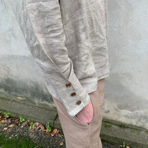 May include: A beige linen shirt with long sleeves and buttoned cuffs. The shirt is tucked into beige linen pants.