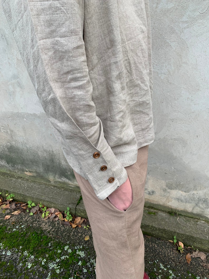 May include: A beige linen shirt with long sleeves and buttoned cuffs. The shirt is tucked into beige linen pants.