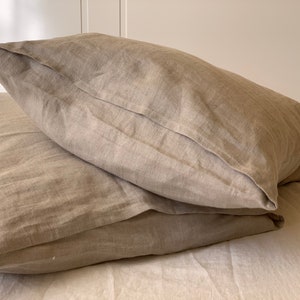 May include: Two beige linen pillowcases stacked on top of each other. The pillowcases are made of a soft, natural fabric and have a subtle texture.
