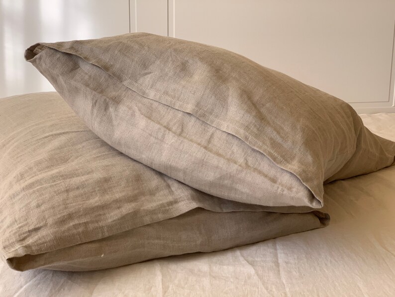 May include: Two beige linen pillowcases stacked on top of each other. The pillowcases are made of a soft, natural fabric and have a subtle texture.
