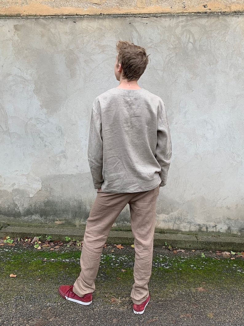 May include: A person wearing a light brown linen shirt and matching pants. The shirt has long sleeves and a relaxed fit. The pants are straight-leg and have a casual look.