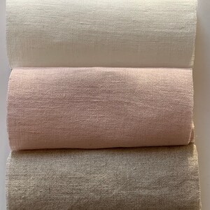 May include: Three rolls of fabric in different colors: white, light pink, and light brown. The fabric has a linen texture.