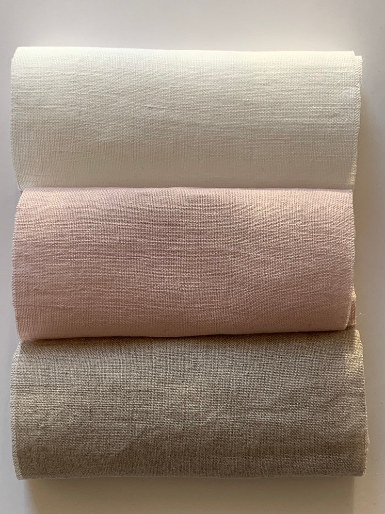May include: Three rolls of fabric in different colors: white, light pink, and light brown. The fabric has a linen texture.