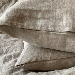 May include: Two beige linen pillowcases stacked on top of each other. The pillowcases are made of a soft, natural fabric and have a subtle texture.