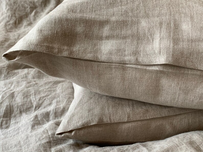 May include: Two beige linen pillowcases stacked on top of each other. The pillowcases are made of a soft, natural fabric and have a subtle texture.