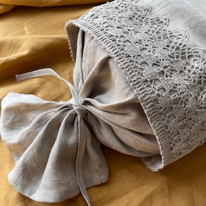 May include: A beige linen pillow with a decorative crocheted lace trim. The pillow is tied with a matching fabric bow. The background is a solid mustard yellow.