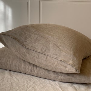 May include: Two beige linen pillowcases stacked on top of each other. The pillowcases are made of a soft, natural fabric and have a subtle texture.