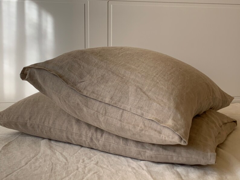May include: Two beige linen pillowcases stacked on top of each other. The pillowcases are made of a soft, natural fabric and have a subtle texture.
