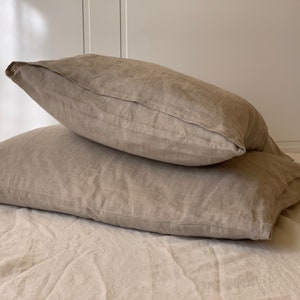 May include: Two beige linen pillowcases stacked on top of each other. The pillowcases are made of a soft, natural fabric and have a subtle texture.