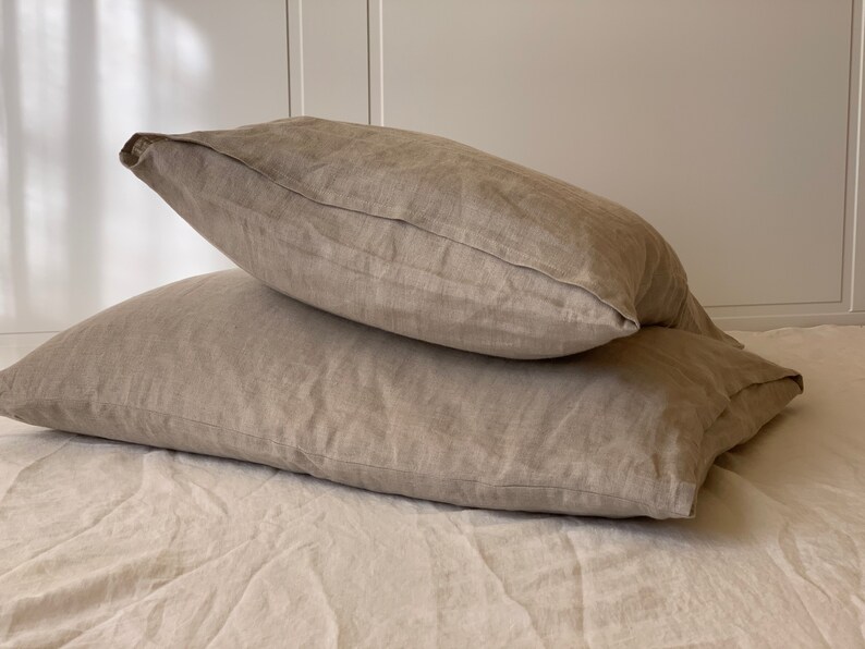 May include: Two beige linen pillowcases stacked on top of each other. The pillowcases are made of a soft, natural fabric and have a subtle texture.