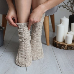Puede incluir: Un par de calcetines de punto beige con un patr&oacute;n de encaje. Los calcetines se est&aacute;n subiendo en las piernas de una persona.