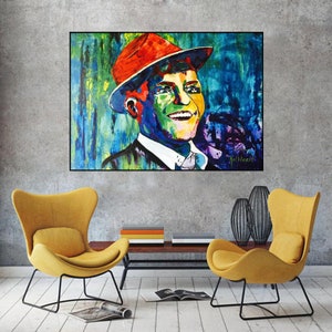 May include: A rectangular wall art print featuring a vibrant, multi-colored pop art portrait of a smiling person wearing a fedora hat. The artwork uses bold strokes of blue, green, yellow, and red, with a signature visible in the bottom right corner.
