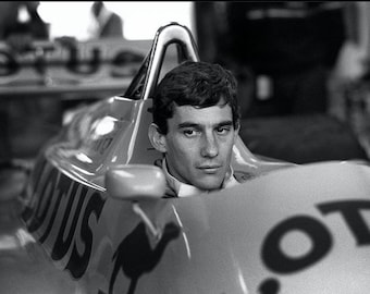 Puede incluir: Una foto en blanco y negro de un piloto de carreras con un traje de carreras y un casco, sentado en un coche de carreras. El coche tiene la palabra "Lotus" en el lateral.