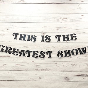 May include: Black banner with the text "This is the Greatest Show!" hanging on a white wood background.
