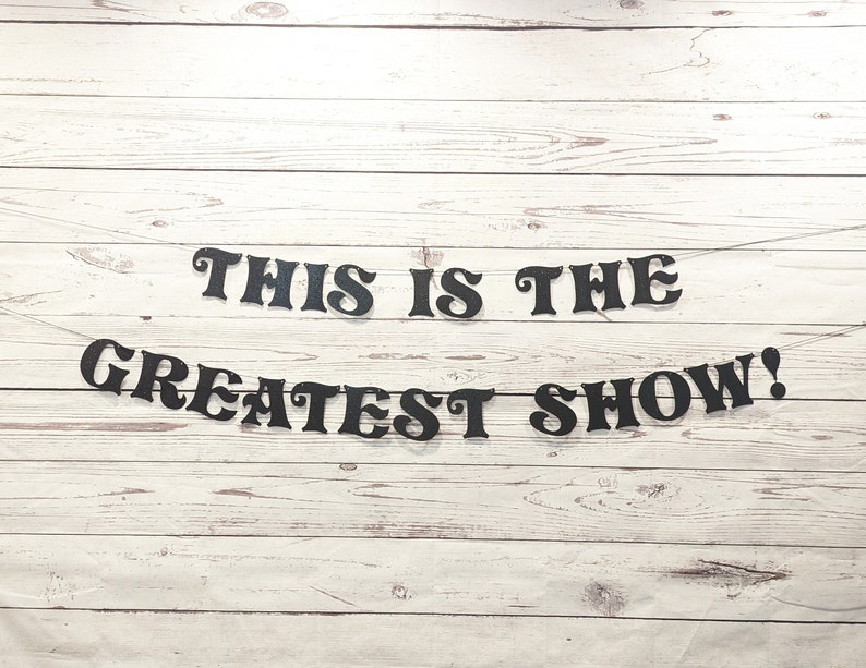 May include: Black banner with the text "This is the Greatest Show!" hanging on a white wood background.