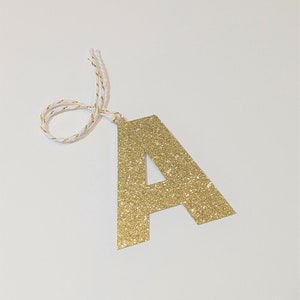 May include: Gold glitter letter A ornament with a white twine string.