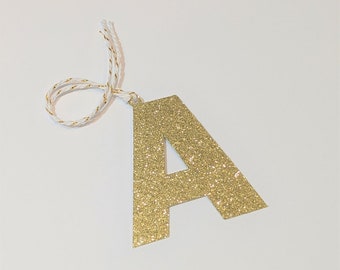 May include: Gold glitter letter A ornament with a white twine string.