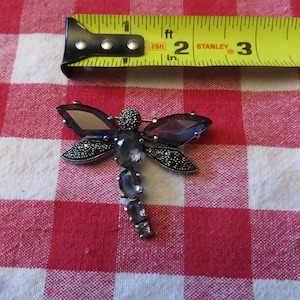 May include: A silver dragonfly brooch with purple and clear faceted glass stones and marcasite accents.