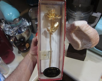 May include: A real rose preserved in 24K gold, displayed in a clear box with a red border. The box has a label that reads "Real Rose Preserved in 24K Gold".