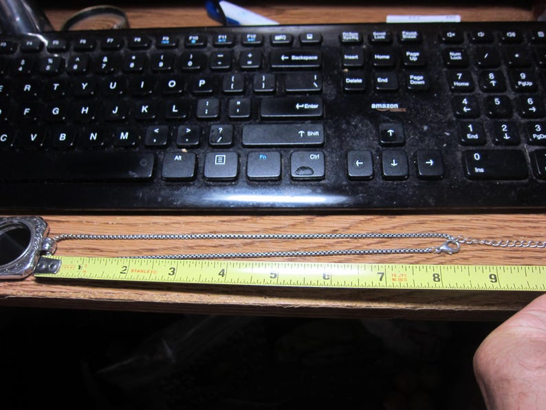 Pu&ograve; includere: Una collana argentata con un ciondolo decorativo e una catena a scatola. La collana &egrave; misurata con un metro a nastro giallo, che mostra una lunghezza di circa 23 cm.