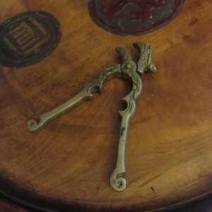 May include: A brass nutcracker with a decorative design. The nutcracker is in the shape of a pair of pliers with a decorative design on the handles.