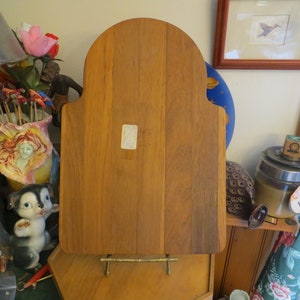 May include: A wooden cutting board with a rounded top and a stand. The board is made of light brown wood and has a natural finish.