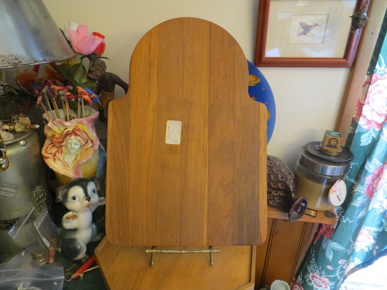 May include: A wooden cutting board with a rounded top and a stand. The board is made of light brown wood and has a natural finish.