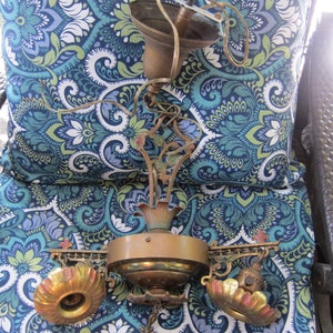 May include: Antique brass chandelier with ornate floral details and three light fixtures. The chandelier is disassembled and lying on a blue and green patterned fabric.
