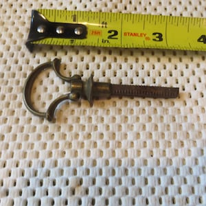 May include: A brass key with a decorative handle and a threaded shaft. The key is approximately 2 inches long.