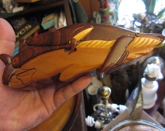 May include: A wooden puzzle box shaped like a dolphin. The box is made of light and dark wood and has a natural finish. The dolphin's body is carved with intricate details.