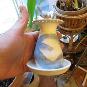 May include: A ceramic vase with a blue and white landscape design. A small bird figurine sits on the top of the vase.