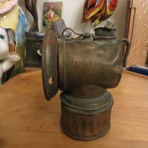 May include: A vintage brass miners lamp with a round,  bulbed base and a handle. The lamp has a  circular reflector and a  brass  cap with the text "SAFETY FIRST" embossed on it.