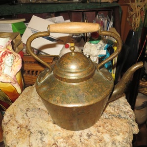May include: A vintage copper teapot with a wooden handle and brass accents. The teapot has a patina finish and is in good condition.