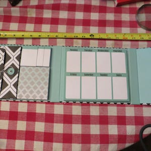 May include: A blue and white weekly planner with a notepad section, a section for sticky notes, and a section for notes. The planner has a black and white geometric pattern on the cover.